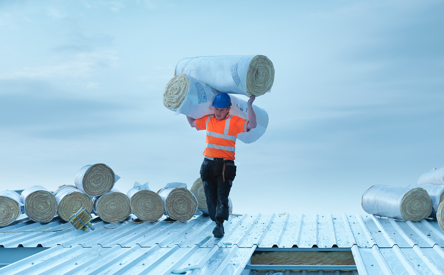 Ouvrier transportant des rouleaux d'isolant à installer dans le toit de l'usine