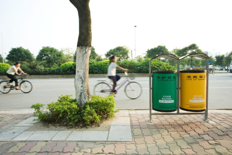 Cyclists riding in street behind recycling bins in Guangdong Province, Guangzhou