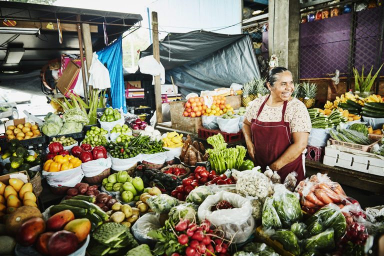 Lachende weibliche Obst- und Gemüseverkäuferin, die am Stand auf dem Marktplatz arbeitet