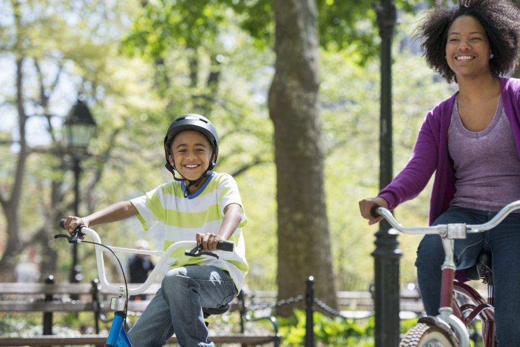 US: A family in the park on a sunny day. A mother and son cycling on a path.