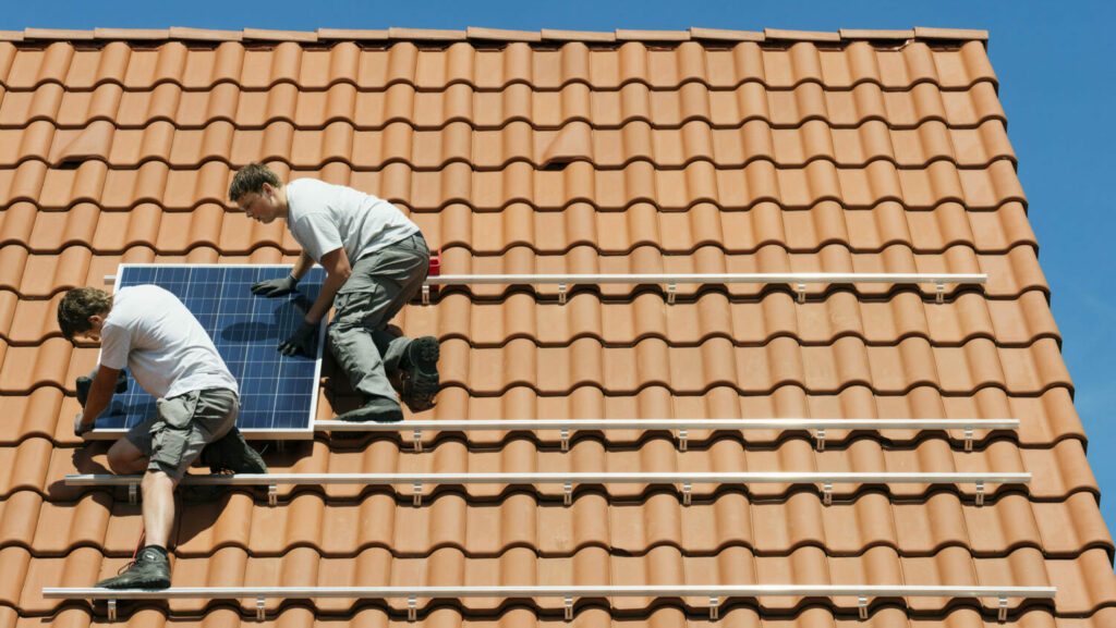 Workers installing solar panel on roof framework of new home, Netherlands