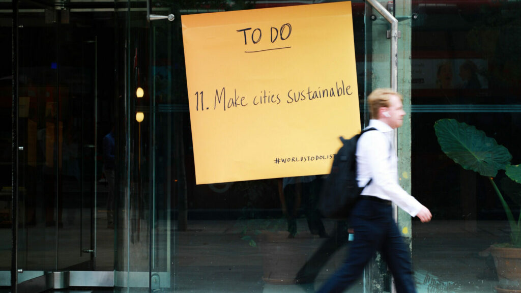 A man walks by a poster for the “World’s To-Do List” campaign launch event, featuring a campaign sticky note that reads "TO DO: Make cities sustainable."