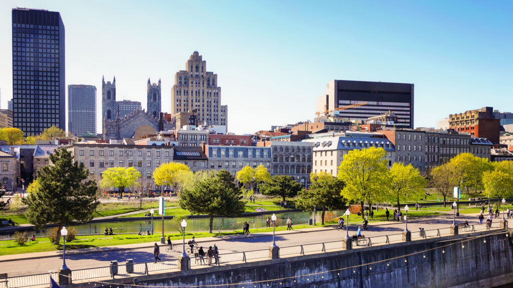 Vieux port de Montreal and downtown skyline with promenade pier on a clear May Springtime day with people walking in the distance.