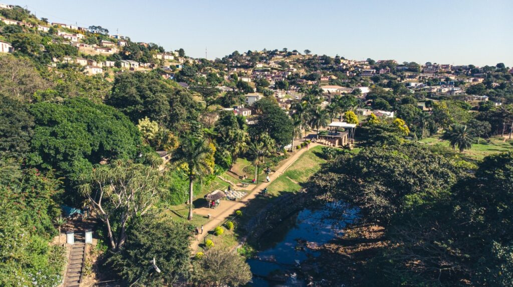 Riverine restoration programme in Durban (eThekwini). The photo shows a riverside scene with trees, homes and people enjoying a community space. Photo courtesy of Durban eThekwini Metropolitan Municipality.