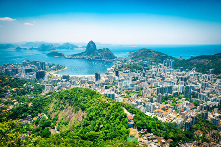Photo of the city of Rio de Janeiro, with green hilltops, and the ocean present.